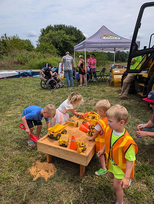 children playing near sandbox outside Comer Construction tent at the Touch a Truck event